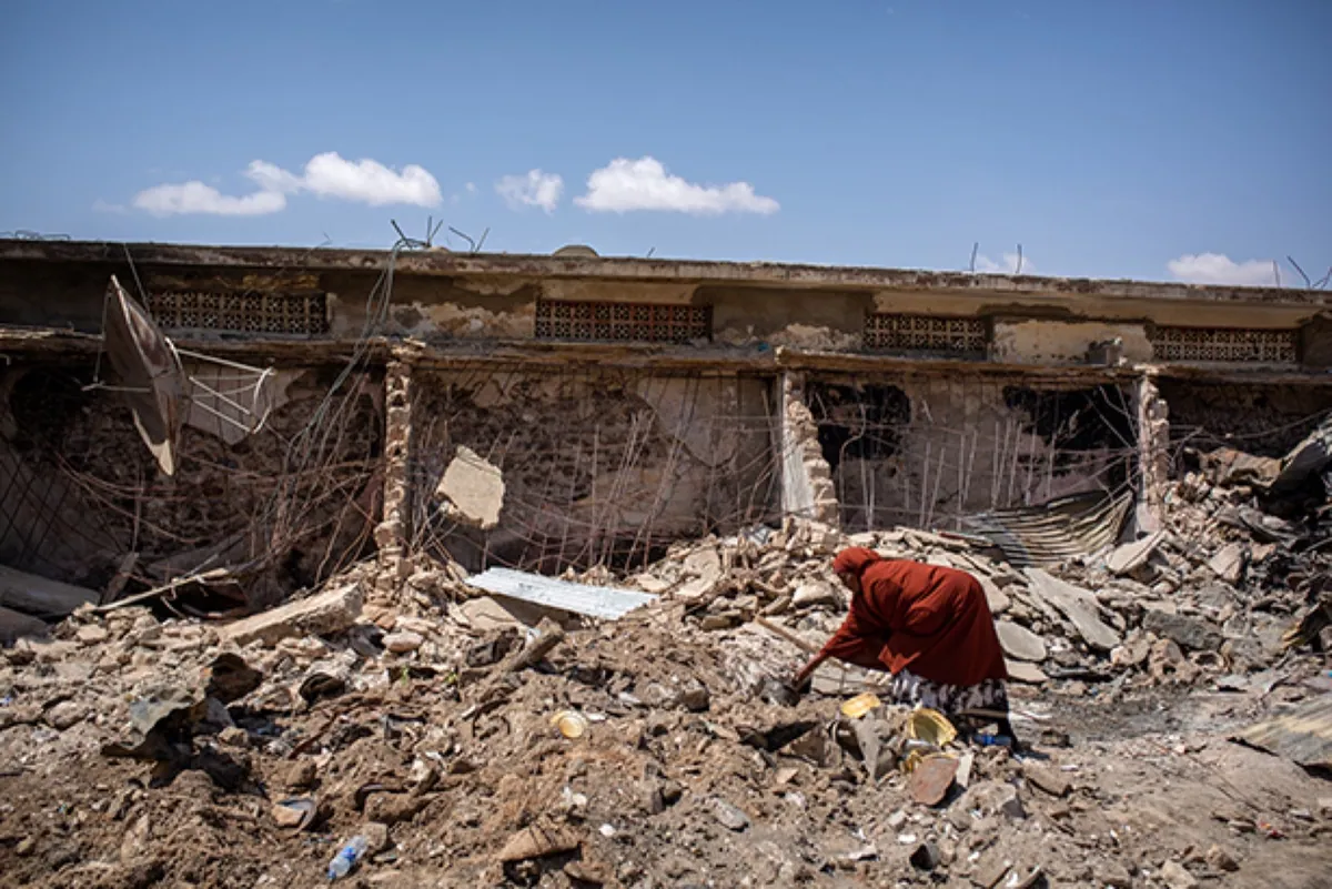 The Guardian, photo 04. A woman picks through the burnt remains at the market.