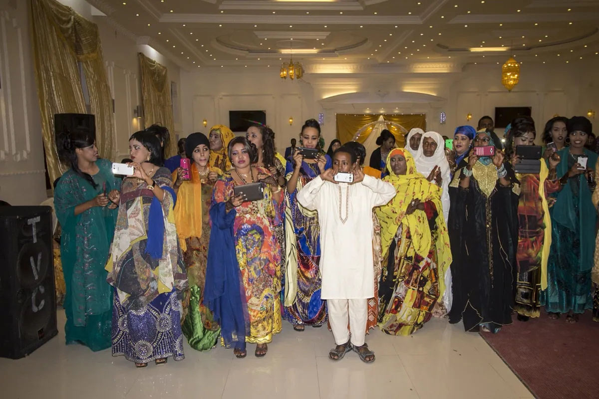 Division Multiplied, photo 05. Guests at a wedding party take photos as the bride and groom arrive.